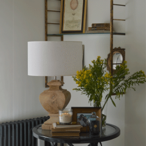 Un rincón junto al sofá une piezas antiguas y actuales. Una lámpara de madera, estantería rescatada y flores componen una escena casi pictórica.