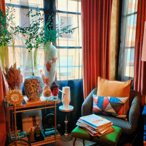 Rincón de lectura: cortinas de terciopelo, lámpara dorada y sillón tapizado con libros al pie.