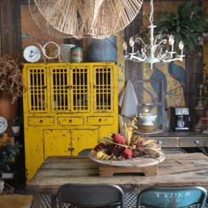 El comedor con la alacena amarilla y fondo de pavos reales. Vajilla, flores secas y luz cálida.